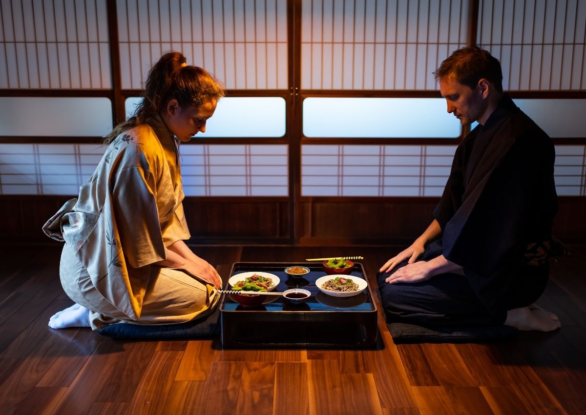 Ungt par sitter på gulvet og spiser et tradisjonelt japansk måltid