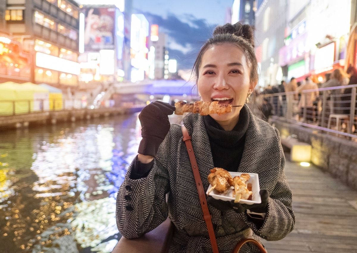 Kvinne som spiser gatemat langs vannet i en japansk storby