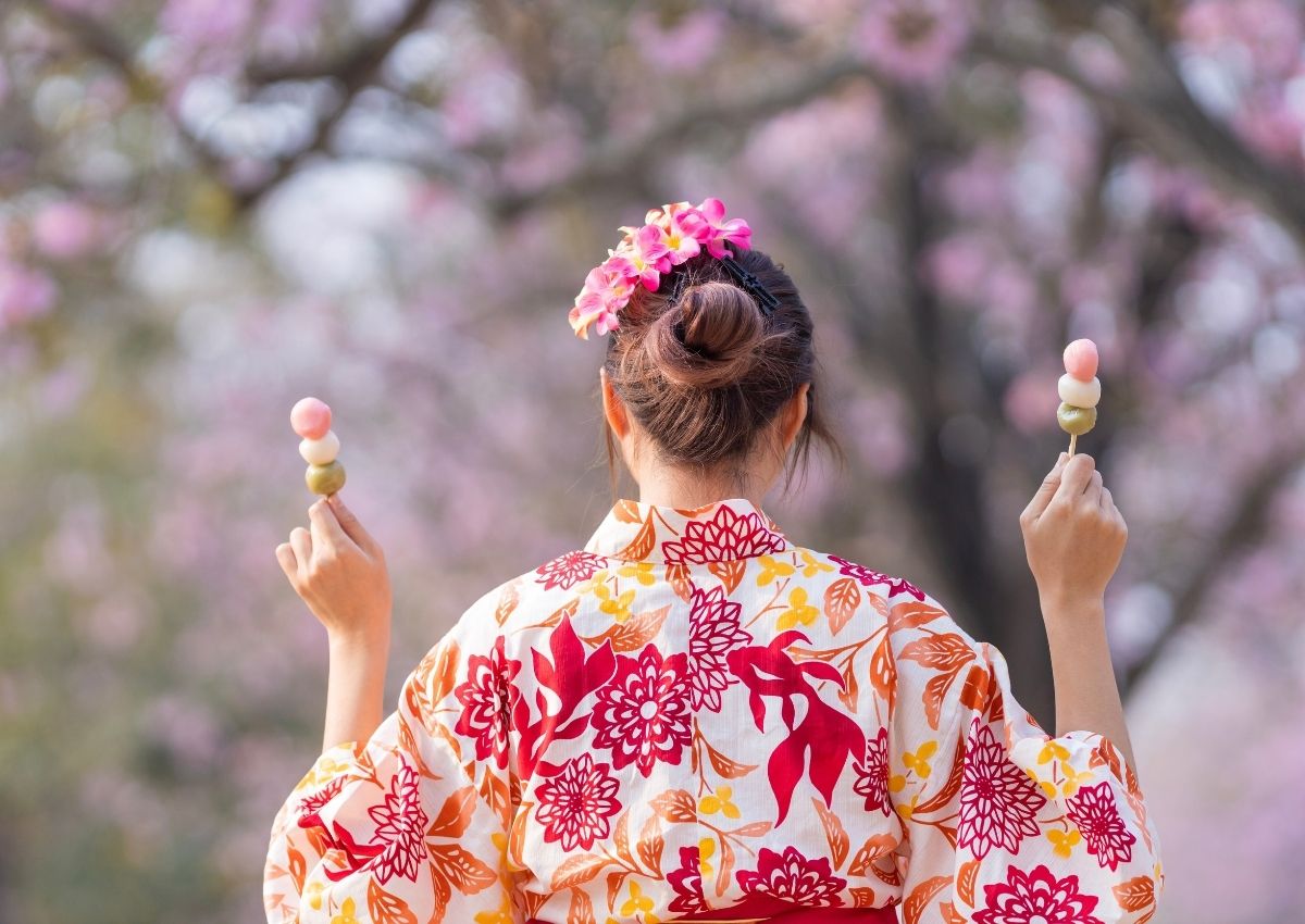 Japansk kvinne står med ryggen til kameraet i kimono, og holder oppe to hanami-søtsaker.
