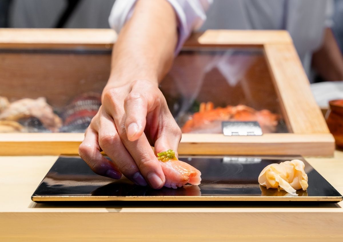 En japansk sushikokk legger en fersk sushibit på en tallerken.