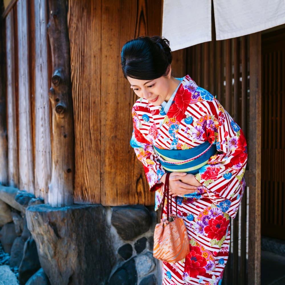 Japansk kvinne i fargerik kimono bukker foran en tradisjonell trebygning i Kyoto