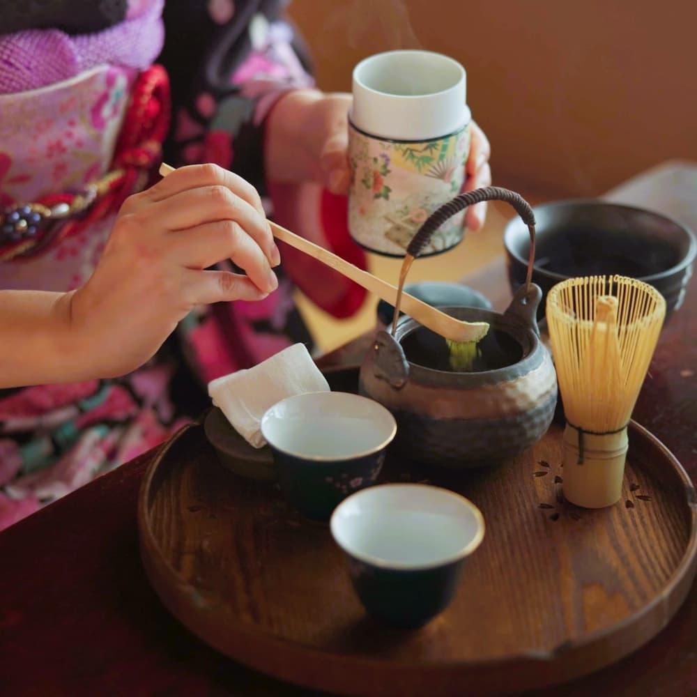 Japansk kvinne tilbereder matcha-te i en tradisjonell teseremoni hjemme, med matchapulver, urter og tekanne