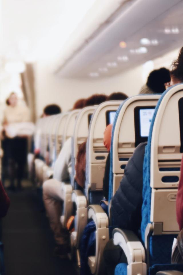 Interiør i et stort passasjerfly med folk som sitter og en flyvertinne i uniform som går ned midtgangen