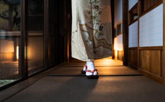 Kvinne i kimono går gjennom en tradisjonell ryokan med tatamimatter og shoji-dører