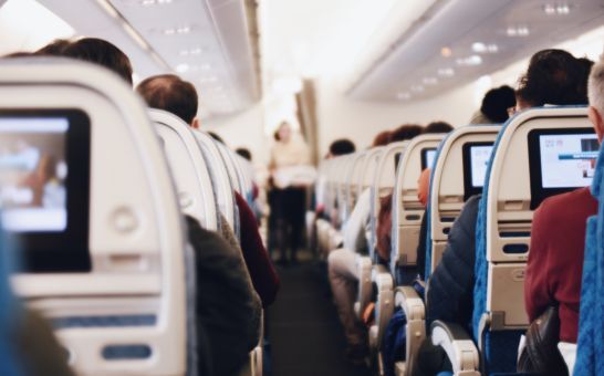 Interiør i et stort passasjerfly med folk som sitter og en flyvertinne i uniform som går ned midtgangen