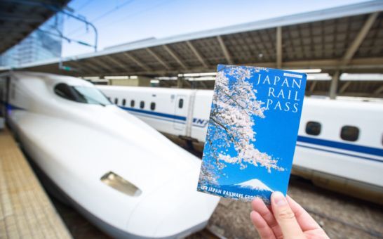 Hånden holder en Japan Rail Pass-billett foran en Shinkansen på Tokyo stasjon
