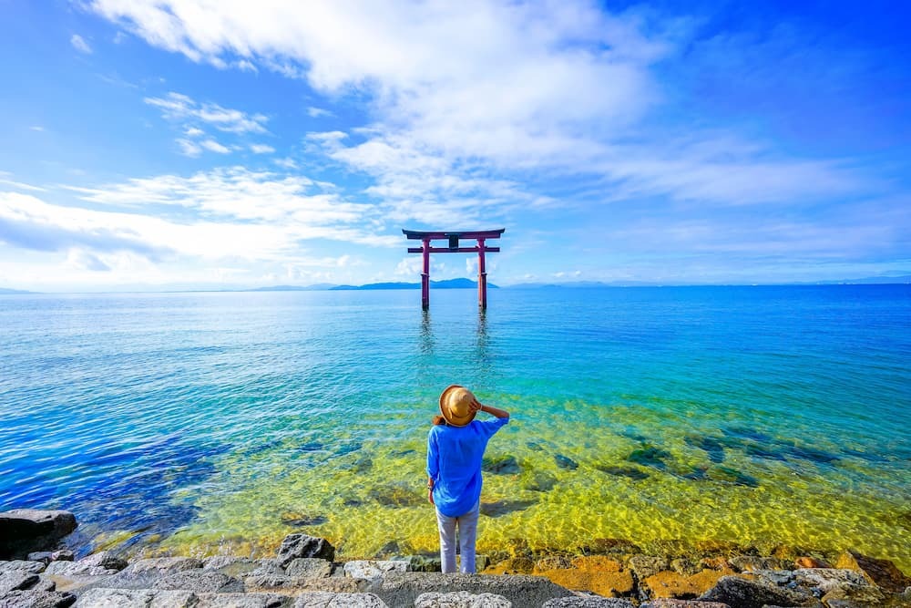 Reisende står nær en torii-port ved Biwa-sjøen i Shiga-prefekturet i Japan