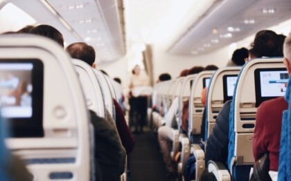 Interiør i et stort passasjerfly med folk som sitter og en flyvertinne i uniform som går ned midtgangen